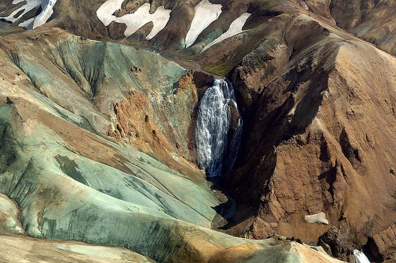 Island: Wasserfall zwischen grünen und roten Felsen