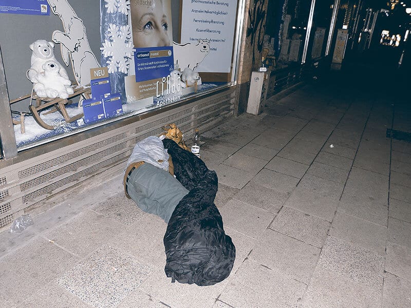 Obdachloser auf der Straße ist zu unterkühlt und betrunken um in seinen Schlafsack zu kriechen